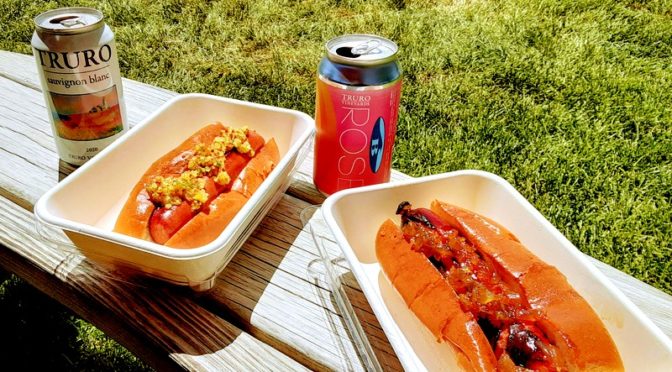 Canned wines and hot dogs sit on a wooden table